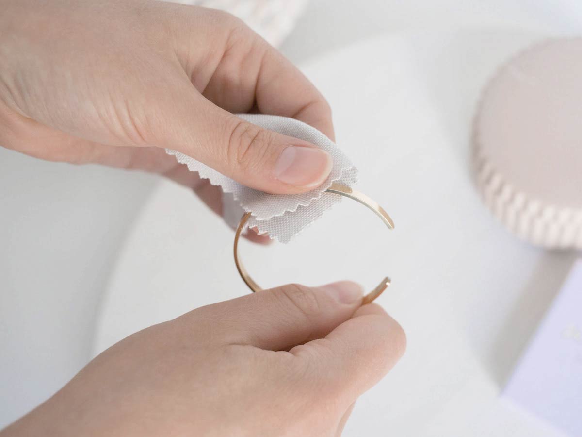 Handmodel zeigt wie man einen hochwertigen Modeschmuck Armreif mit Gravur in Gold von Oh Bracelet Berlin reinigen kann mit einem einfachen weichen Poliertuch