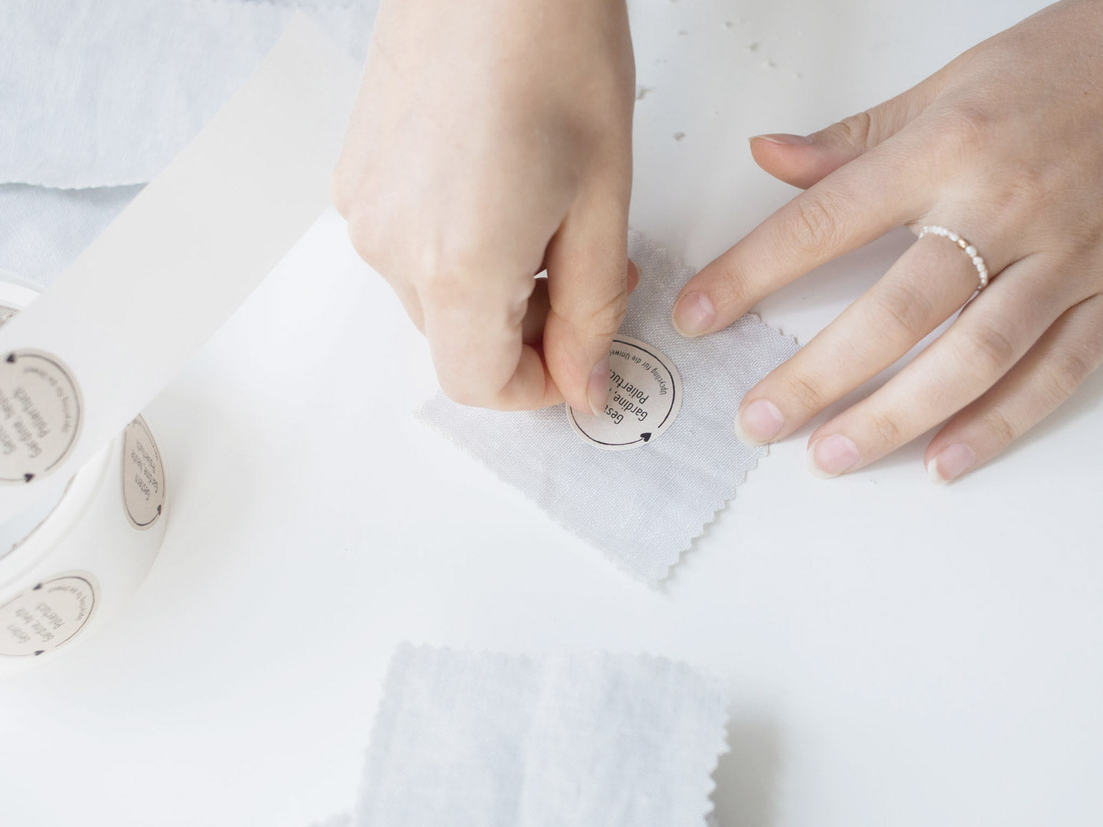 Mitarbeiter versieht selbst hergestellte Upcycling Poliertücher die aus wiederverwendeten Stoffreste von Oh Bracelet berlin selbst hergestellt werden mit einem Sticker 