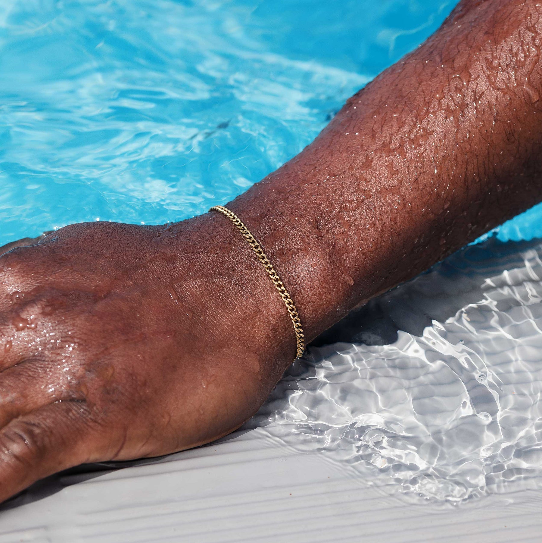 Arm mit einer goldenen Armkette am Pool