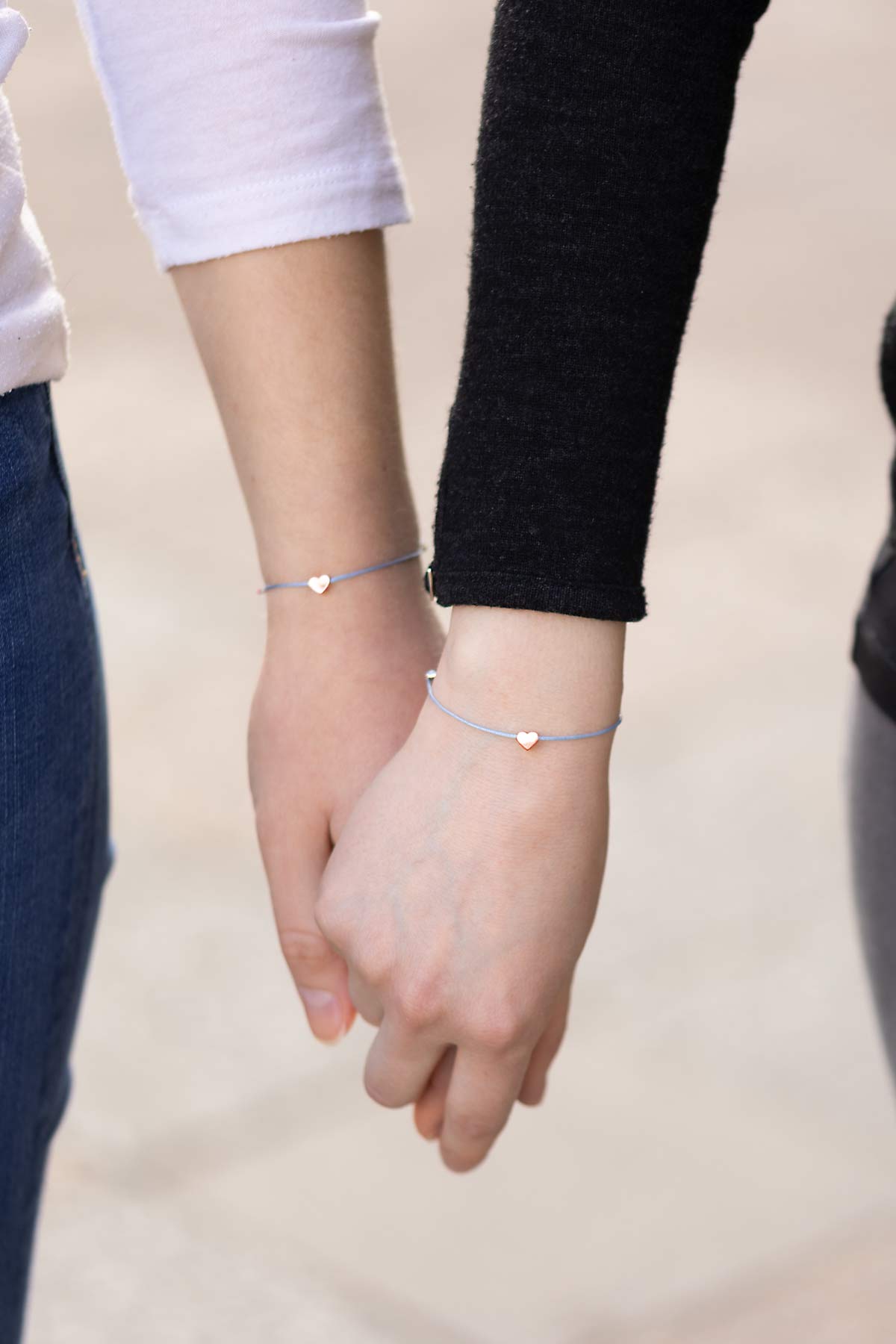 Freundinnen halten Hände und präsentieren Armbänder mit Herz Symbol