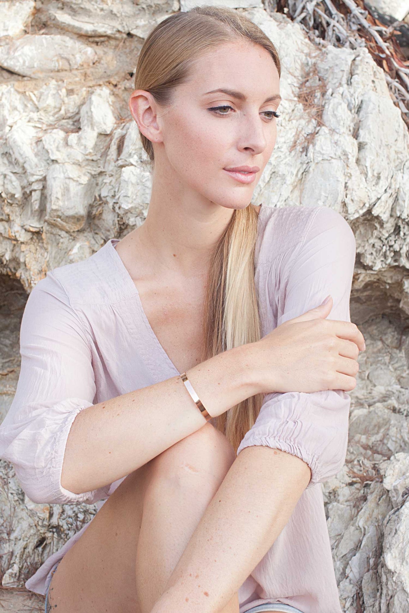 Weibliches Fotomodel zeigt Armreif mit Gravur vor Steinmauer