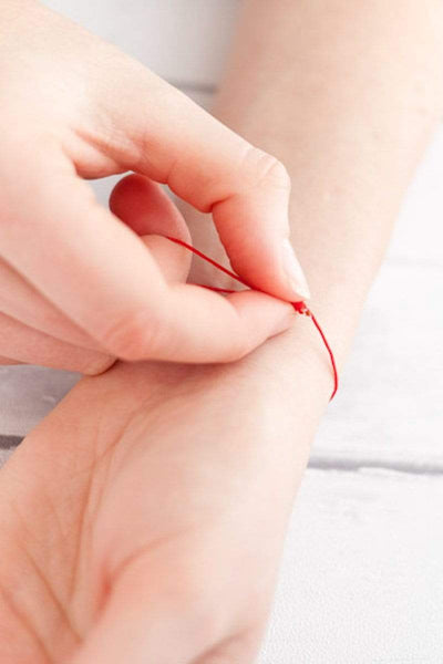 Handmodel präsentiert den Schiebeknoten von einem Armband in der Farbe Kirschrot